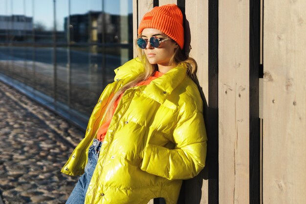 Ritratto di una ragazza alla moda che indossa un puffer giallo e un cappello lavorato a maglia arancione