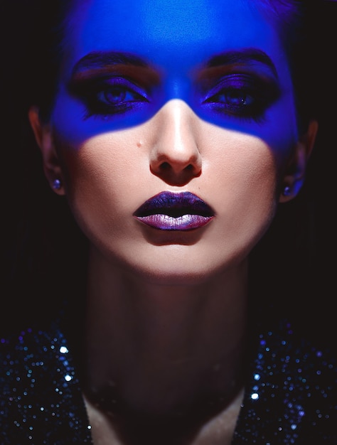 Ritratto di una ragazza alla moda con un trucco elegante e una luce al neon blu sul viso sullo sfondo nero in studio
