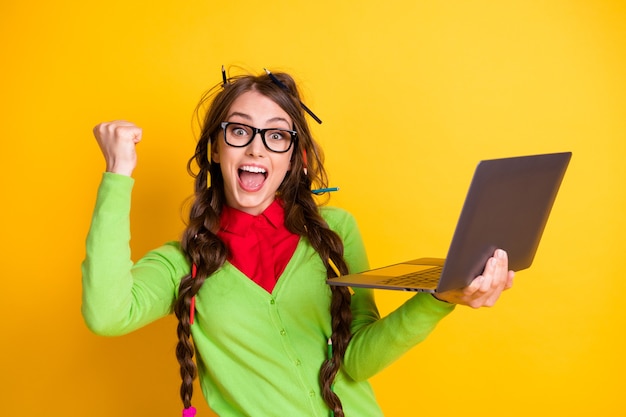 Ritratto di una ragazza allegra e allegra attraente che tiene in mano un computer portatile che celebra il raggiungimento di uno sfondo di colore giallo brillante isolato