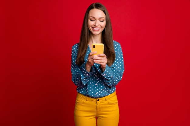 Ritratto di una ragazza allegra e focalizzata attraente che utilizza un gadget del dispositivo in chat isolato con uno sfondo di colore rosso brillante