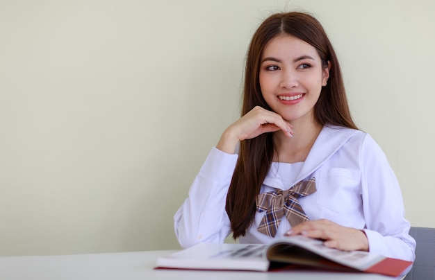 Ritratto di una ragazza asiatica carina e giovane, etnia laotiana, che indossa l'uniforme da studentessa giapponese e coreana, seduto e leggendo un libro con la faccia felice. Concetto di studio della scuola e dell'università.