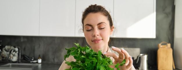 Ritratto di una ragazza attraente con un mazzo di prezzemolo che mangia erbe fresche e verdure che cucinano nel