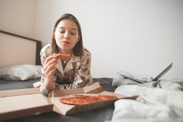 Ritratto di una ragazza attraente sdraiata su un letto con una scatola di pizza