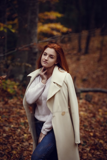 Ritratto di una ragazza bella, sognante e triste con i capelli rossi in camice bianco in autunno