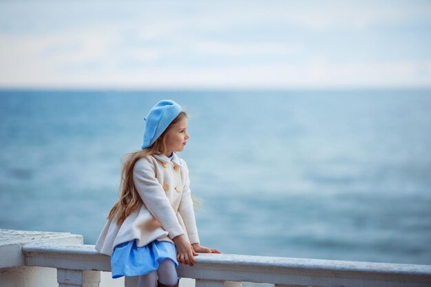 Ritratto di una ragazza bionda con un cappello che guarda il mare freddo