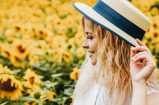 Ritratto di una ragazza bionda con un cappello sul campo di girasoli.