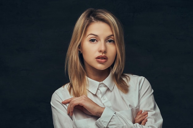 Ritratto di una ragazza bionda sensuale vestita con una camicia bianca, in posa in uno studio. Isolato su uno sfondo scuro.