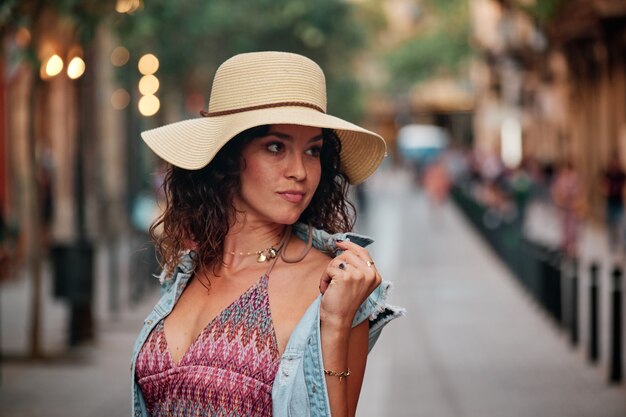 Ritratto di una ragazza bruna con cappello e borsa in posa per un servizio fotografico in una strada della città di Barcellona.