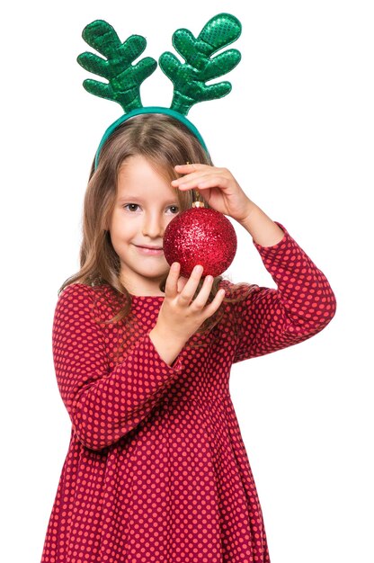 Ritratto di una ragazza caucasica con le buone corna di Natale di un cervo una scolaressa felice isolata su uno sfondo bianco concetto di vacanza divertente bambino carino che tiene una bella palla di Natale