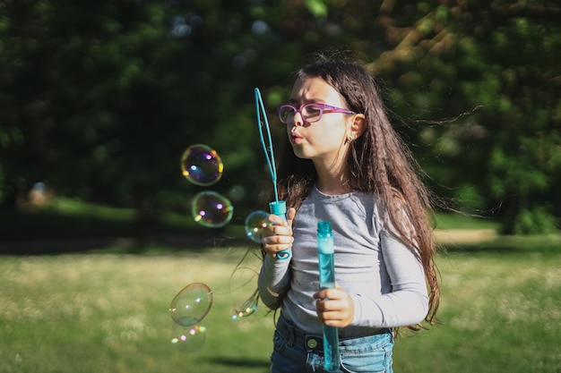 Ritratto di una ragazza caucasica soffia bolle di sapone mentre si trova in un parco su un prato parco giochi