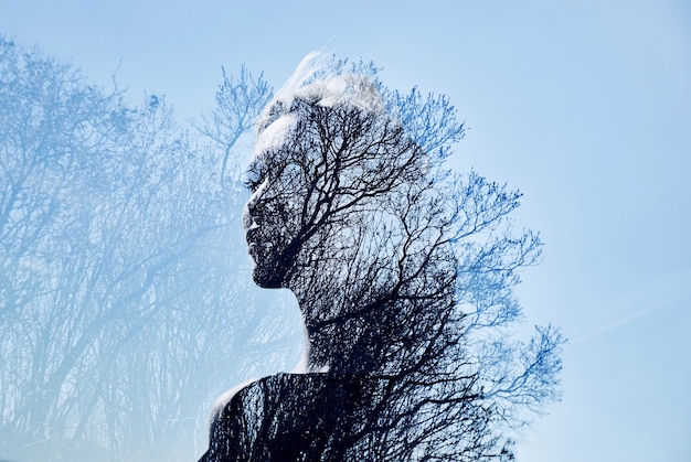Ritratto di una ragazza con doppia esposizione contro una corona d'albero. Delicato e misterioso ritratto di una donna con un cielo azzurro