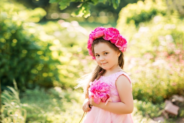 Ritratto di una ragazza con fiori rosa. Una corona di peonie sulla testa del bambino..