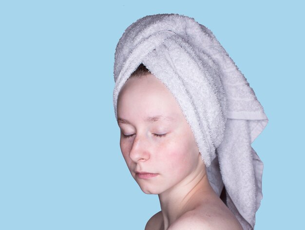 Ritratto di una ragazza con gli occhi chiusi con un asciugamano sulla testa tutta la faccia senza trucco isolata su uno sfondo blu
