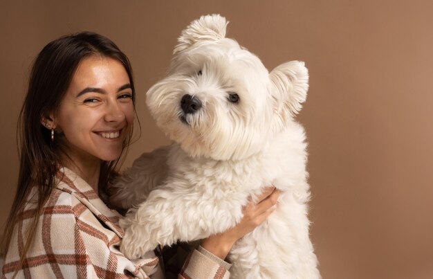 ritratto di una ragazza con un cane bianco West Highland White Terrier su uno sfondo marrone.