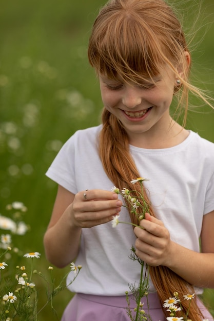 Ritratto di una ragazza con una maglietta bianca su un campo fiorito di margherite con una camomilla in mano Divinazione della camomilla Un campo di margherite in una giornata estiva Messa a fuoco selettiva