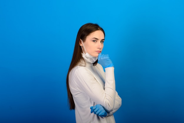 Ritratto di una ragazza con una maschera medica, che indossa un guanto di gomma. Sfondo blu. Copia spazio.
