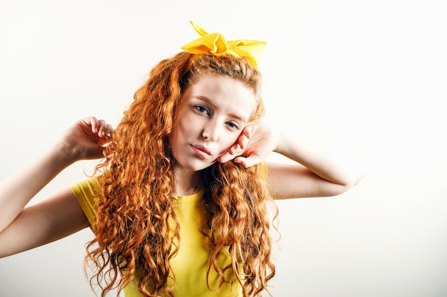 Ritratto di una ragazza dai capelli rossi ricci con un fiocco giallo sulla testa che indossa una maglietta gialla in posa sullo sfondo bianco