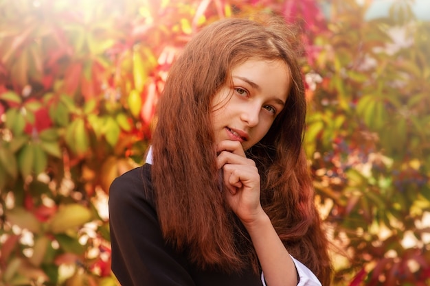 Ritratto di una ragazza di 11 anni con i capelli lunghi in autunno su uno sfondo di foglie rosse. studentessa