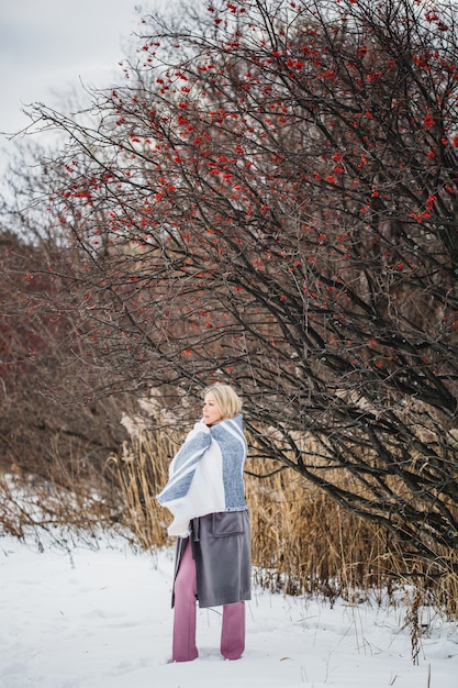 Ritratto di una ragazza di aspetto europeo in una passeggiata invernale, erba, foresta, campo, cappello, salute. Ragazza con un plaid, avvolto in un plaid, sciarpa