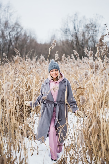 Ritratto di una ragazza di aspetto europeo in una passeggiata invernale, erba, foresta, campo, cappello, salute