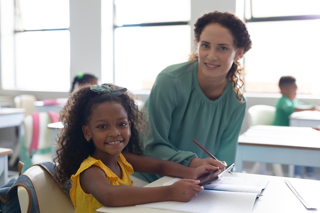 Ritratto di una ragazza elementare afroamericana sorridente con una giovane insegnante caucasica in classe