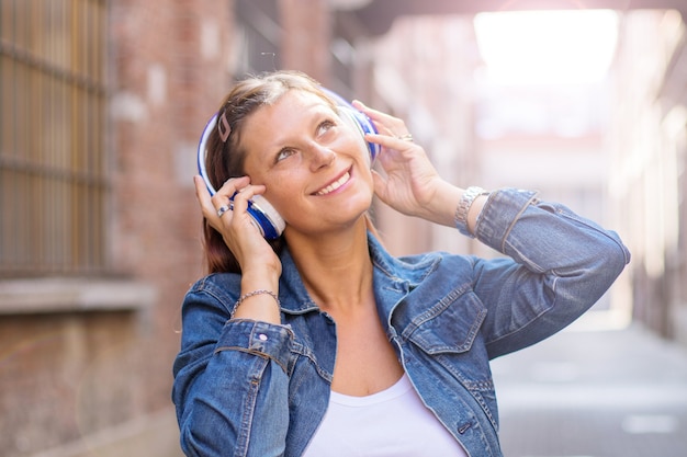 Ritratto di una ragazza felice ascoltando musica con cuffie wireless in strada