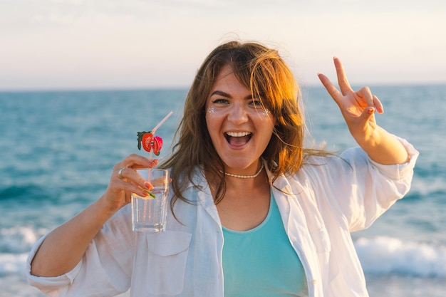 Ritratto di una ragazza felice con un cocktail in mano su uno sfondo di mare bellissimo