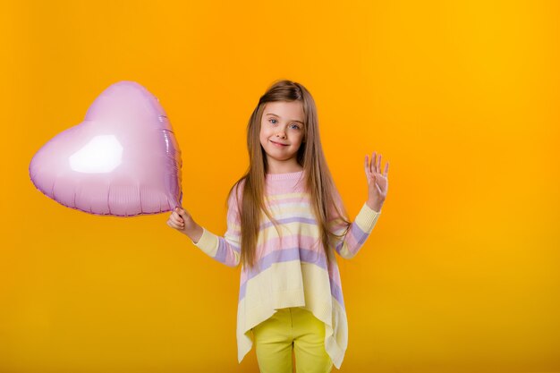 Ritratto di una ragazza felice del bambino che sorride tenendo un pallone rosa a forma di cuore