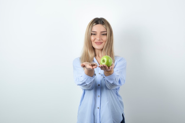 Ritratto di una ragazza felice sorridente che tiene mela verde sopra il muro bianco