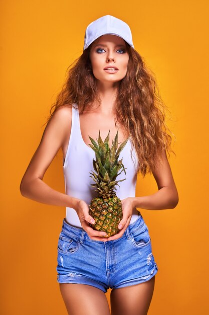 Ritratto di una ragazza giovane e carina in beachwear azienda ananas isolato su sfondo giallo.