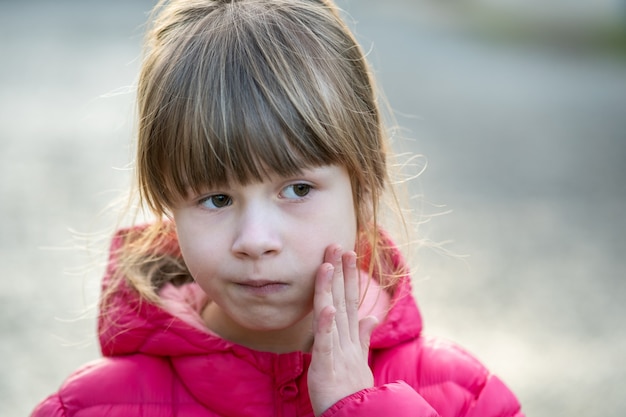 Ritratto di una ragazza graziosa del bambino che tiene la sua mano alla guancia nel dolore all'aperto.