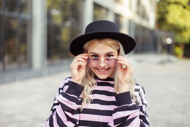 Ritratto di una ragazza hipster carismatica sorridente con occhiali e cappello all'aperto