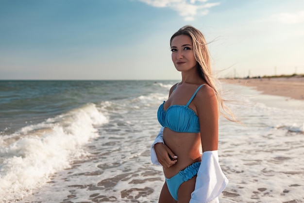 Ritratto di una ragazza in costume da bagno blu e camicia bianca sullo sfondo del mare blu e del cielo limpido