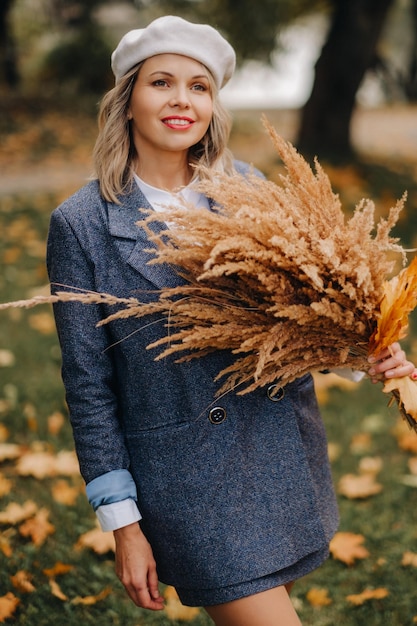 Ritratto di una ragazza in giacca e birette con un bouquet autunnale in un parco autunnale