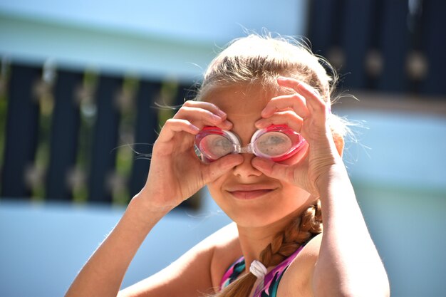 Ritratto di una ragazza in occhiali da nuoto. La ragazza felice nuota nello stagno.