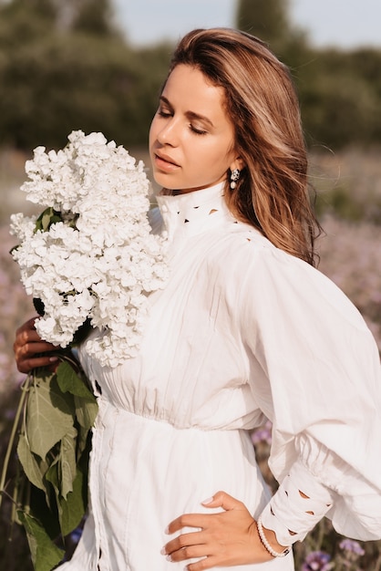 Ritratto di una ragazza in un abito bianco con un mazzo di fiori in estate nella natura nel campo