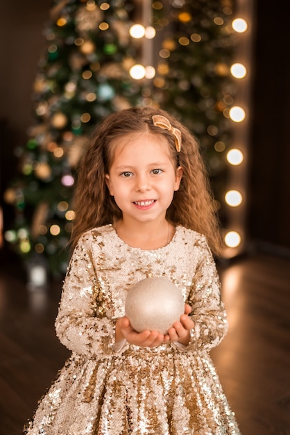 Ritratto di una ragazza in un vestito d'oro sullo sfondo di un albero di Natale..