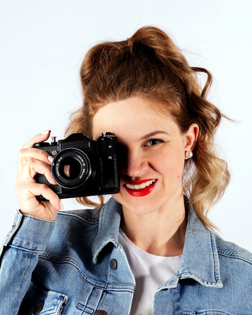 Ritratto di una ragazza retrò sorridente che scatta foto su una fotocamera retrò su sfondo bianco