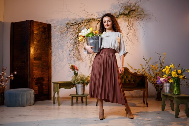 Ritratto di una ragazza riccia con un secchio di tulipani. Contiene fiori freschi e va per belle foto. Foto luminose con fiori in studio