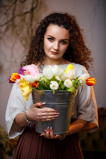 Ritratto di una ragazza riccia con un secchio di tulipani. Fiori freschi per belle foto. Foto delicate con fiori in studio