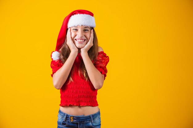 Ritratto di una ragazza sorridente caucasica con un cappello da Babbo Natale su uno sfondo giallo. Natale e concetto di felicità. Chiudi, copia spazio