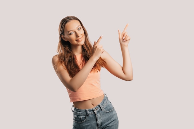 Ritratto di una ragazza sorridente che punta il dito a lato su uno sfondo bianco isolato. La donna positiva indica un'idea, un luogo per la pubblicità