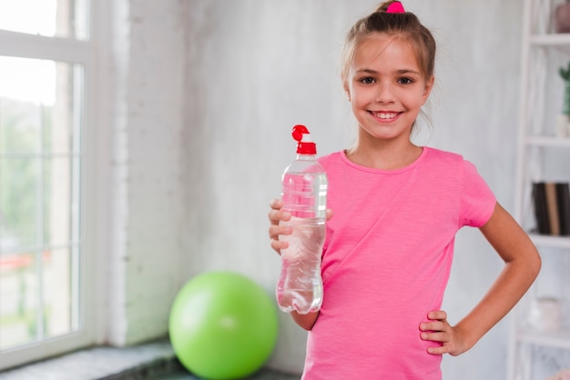 Ritratto di una ragazza sorridente che tiene la bottiglia di acqua di plastica a disposizione