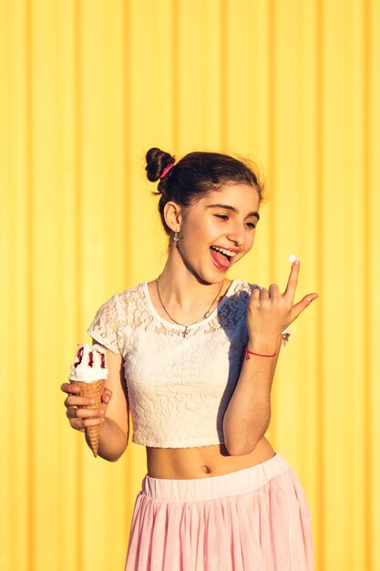 Ritratto di una ragazza sorridente con gelato in mano su un muro giallo. Ragazza alla moda divertendosi.