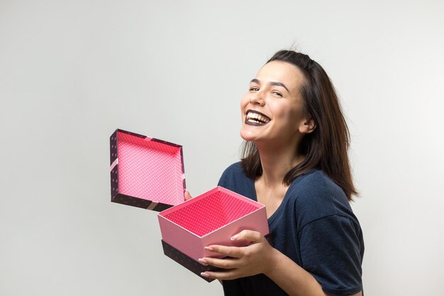 Ritratto di una ragazza sorridente felice che apre una confezione regalo isolata su sfondo bianco