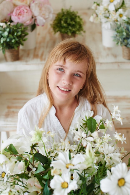 Ritratto di una ragazza sorridente in abito bianco e un mazzo di fiori di margherite