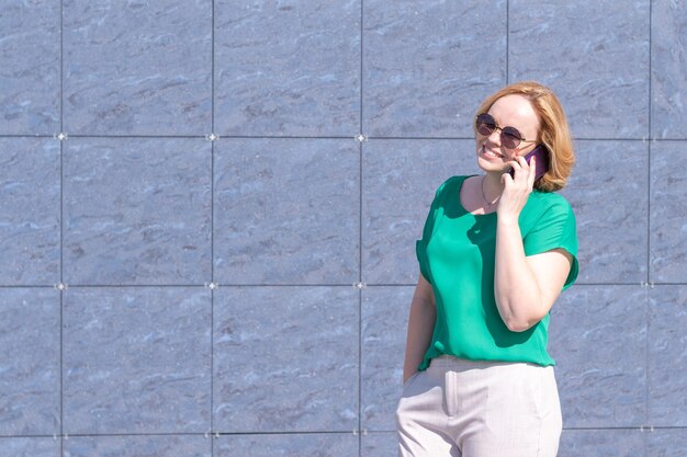 Ritratto di una ragazza sorridente studente che indossa occhiali da sole parlando su un telefono cellulare
