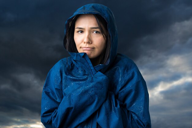 Ritratto di una ragazza sorridente vestita di impermeabile blu in gocce in posa con cappuccio