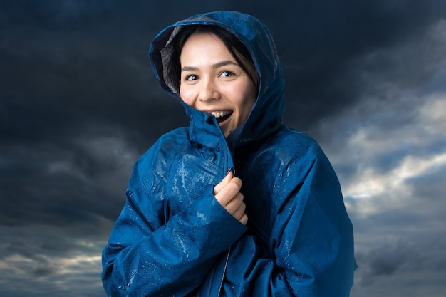 Ritratto di una ragazza sorridente vestita di impermeabile blu in gocce in posa con cappuccio