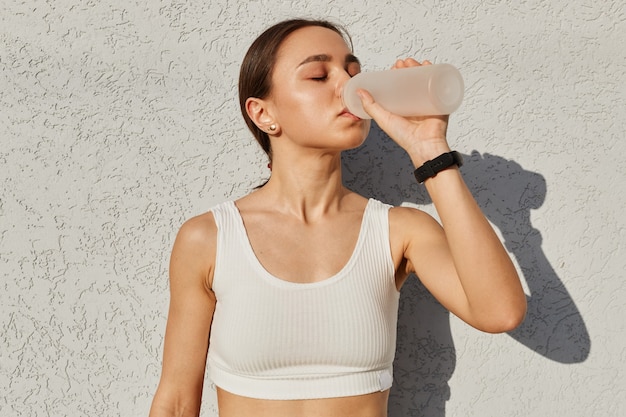 Ritratto di una ragazza stanca che si sente assetata dopo gli esercizi sportivi bevendo acqua dalla bottiglia